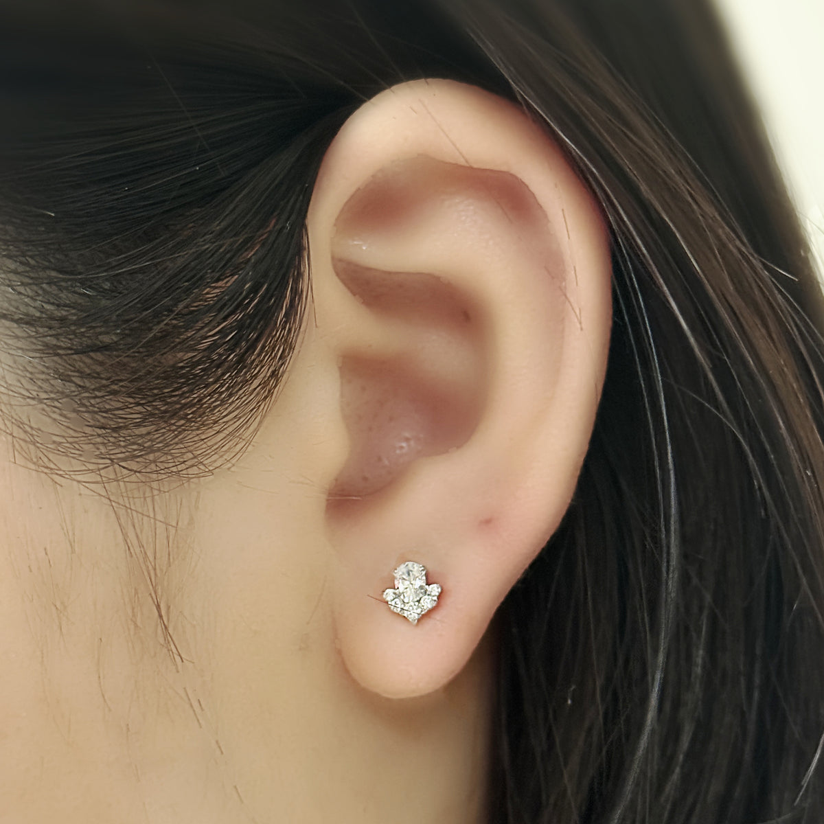 Veil Stud(シルバー)を耳たぶにつけた着用イメージ。楕円の主石を小粒が取り巻く。チタン フラットバックピアス|Rozea