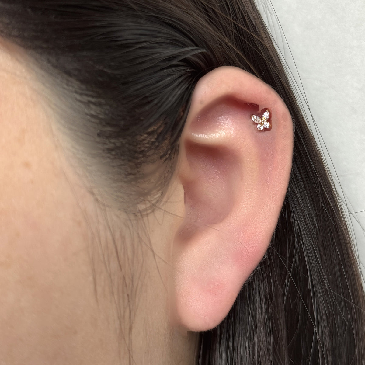 Flutter Stud（ゴールド）を耳の軟骨につけた着用イメージ。小さな蝶のモチーフ。チタン フラットバックピアス｜Rozea