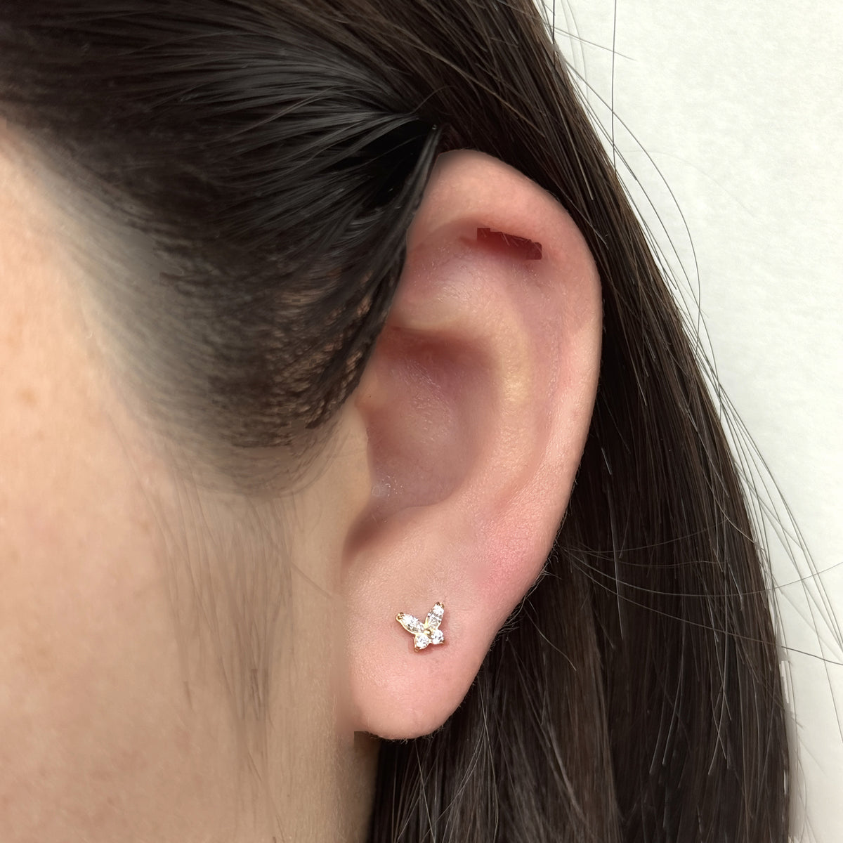 Flutter Stud（ゴールド）を耳たぶにつけた着用イメージ。小さな蝶のモチーフ。チタン フラットバックピアス｜Rozea