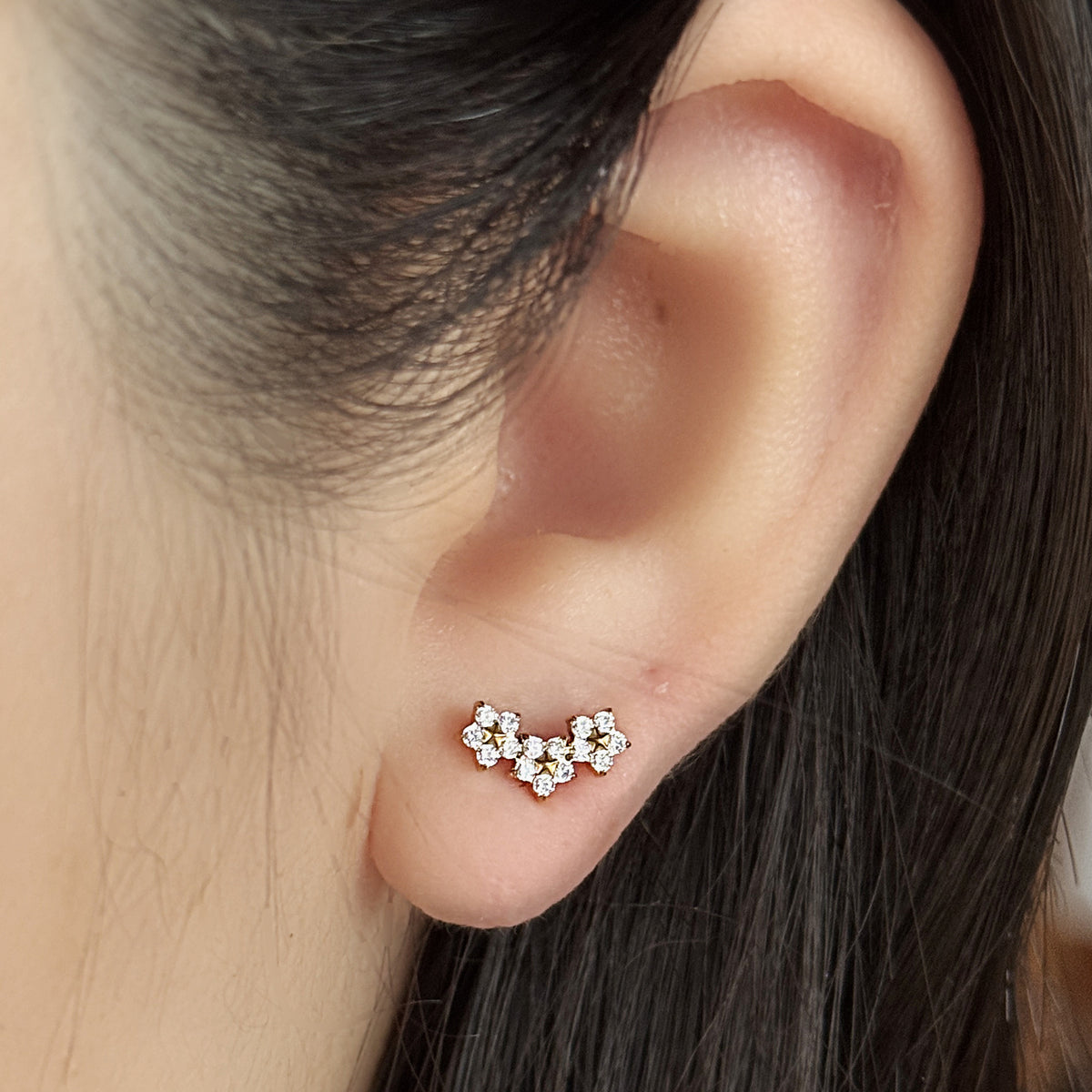 Stella Stud（ゴールド）を耳たぶにつけた着用イメージ。小花の弧が横に流れる。チタン フラットバックピアス｜Rozea