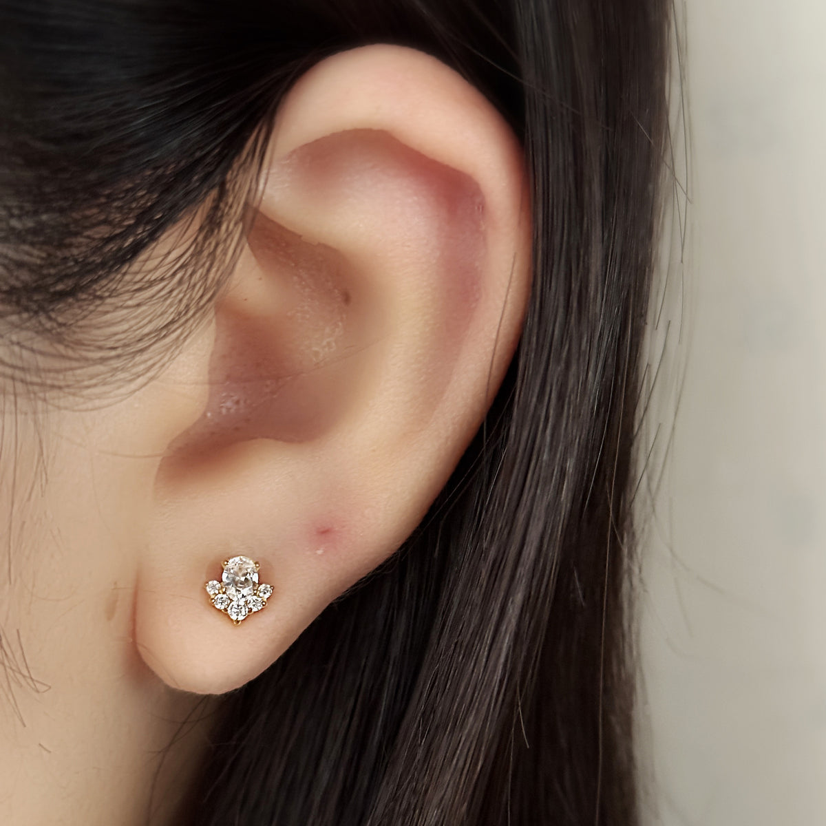 Veil Stud（ゴールド）を耳たぶにつけた着用イメージ。大きな楕円の石をひとつ。チタン フラットバックピアス｜Rozea